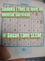 A completed Sudoku puzzle filled in by hand, with neat handwritten numbers inside a 9×9 grid. The page is held at the bottom, and green text over the puzzle reads “Sudoku | This is love of mental survival © Susan Lane SLCM.”